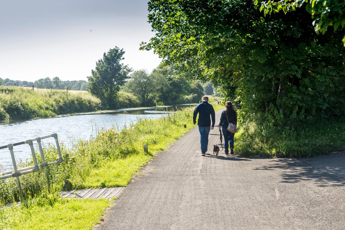 two people walking their dog along the canal footpath