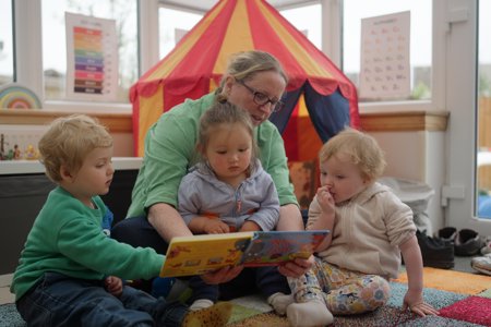 Childminder reading a book with three children