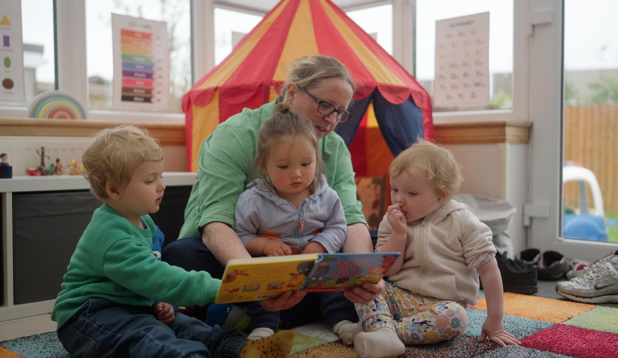 Childminder reading a book with three children