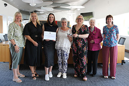 Seven women standing in Council chambers for official photograph.  The woman in the centre is being presented with a framed certificate and a silver quaich. 