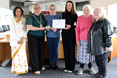 Formal shot of six women standing in Council chambers.  The women in the centre of the pic are holding a framed certificate and a quaich. 