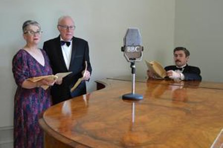 cCast of A Christmas Carol; A Radio Play on Stage standing around a microphone holding scripts 