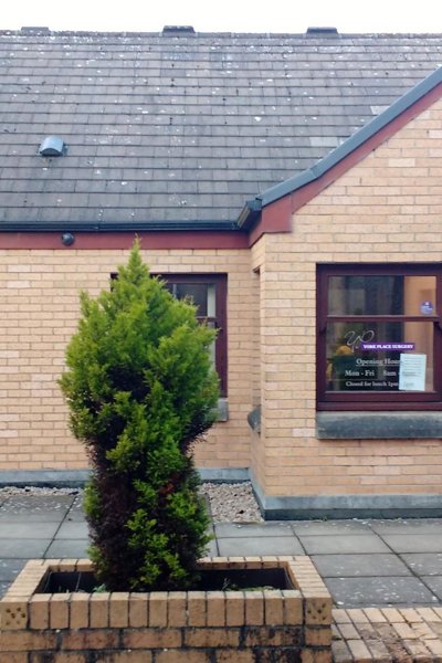 outsude of building showing brick planters with trees and red brick exterior with brown widow frames and door