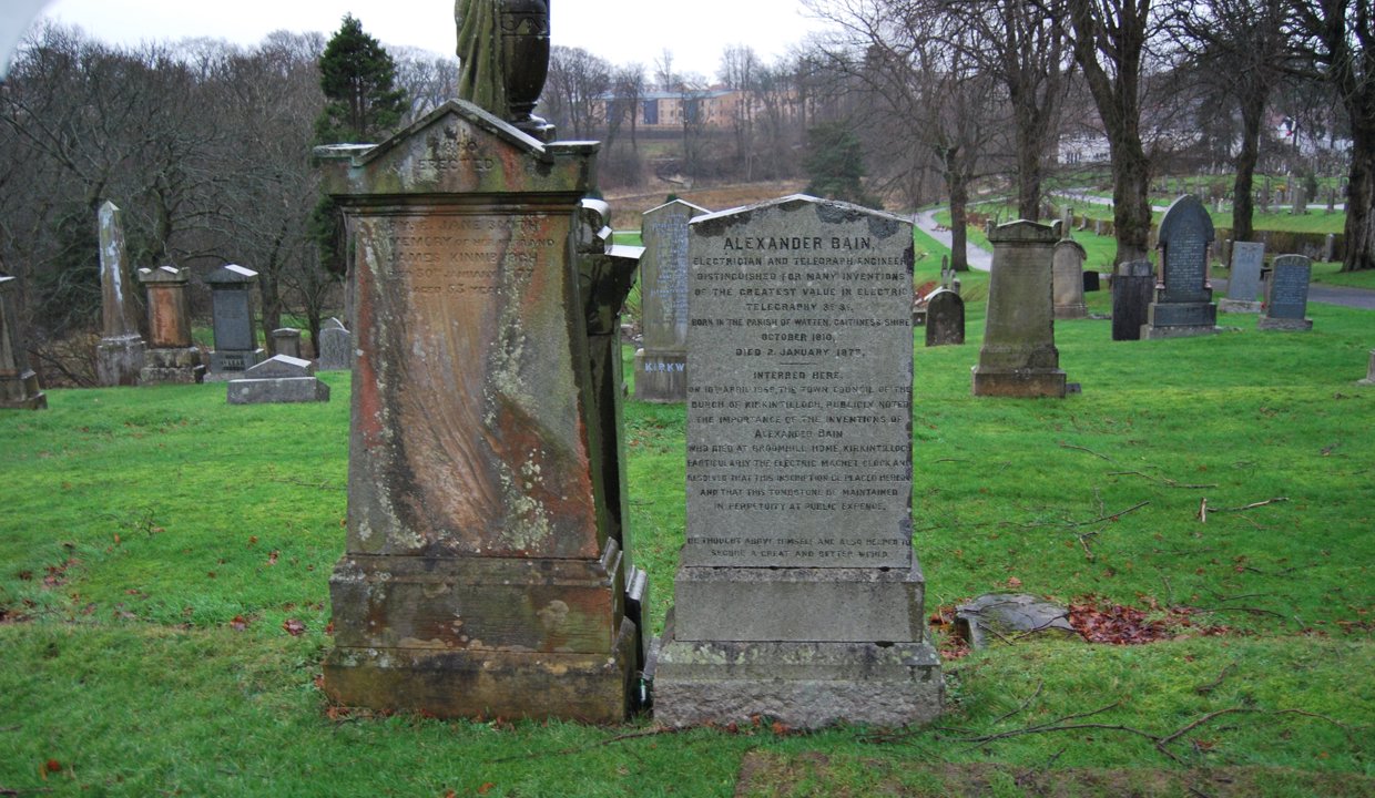 Two headstones in a cemetery with other graves and trees in the background