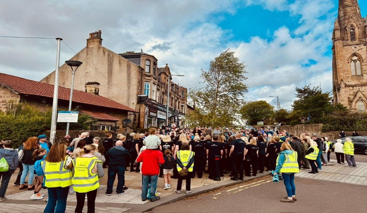 Crowd of people walking up the road of a busy street flanked by people wearing hi vis vests.