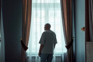 A man is silhouetted against a window, looking out