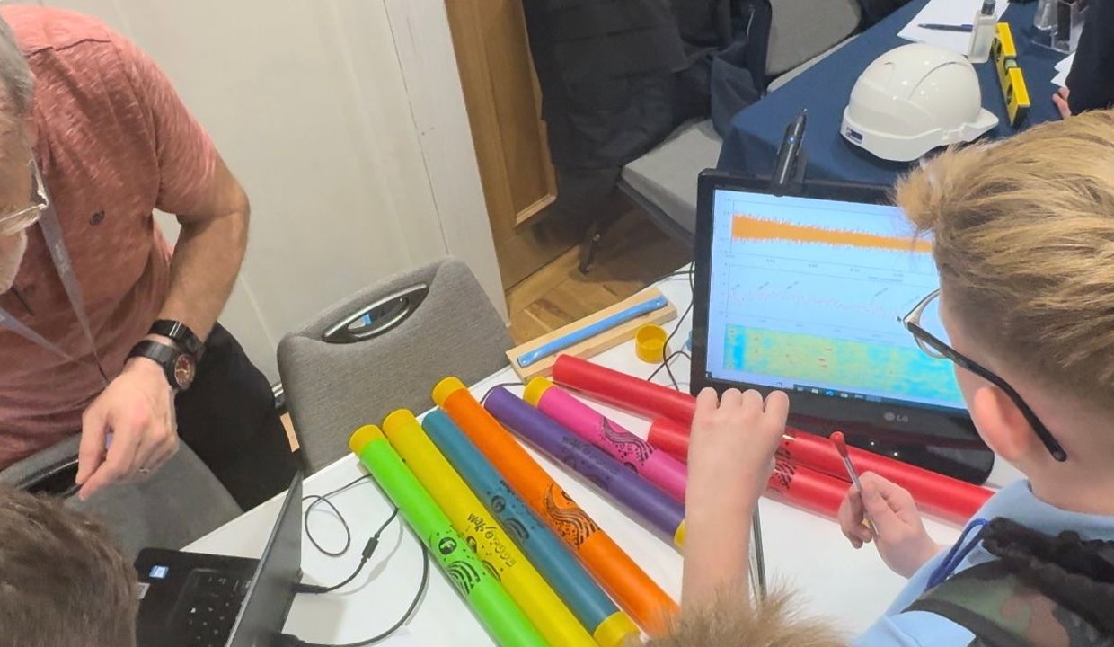 Boy looking at computer screen showing analytics. In front of him are a number of brightly coloured tubes