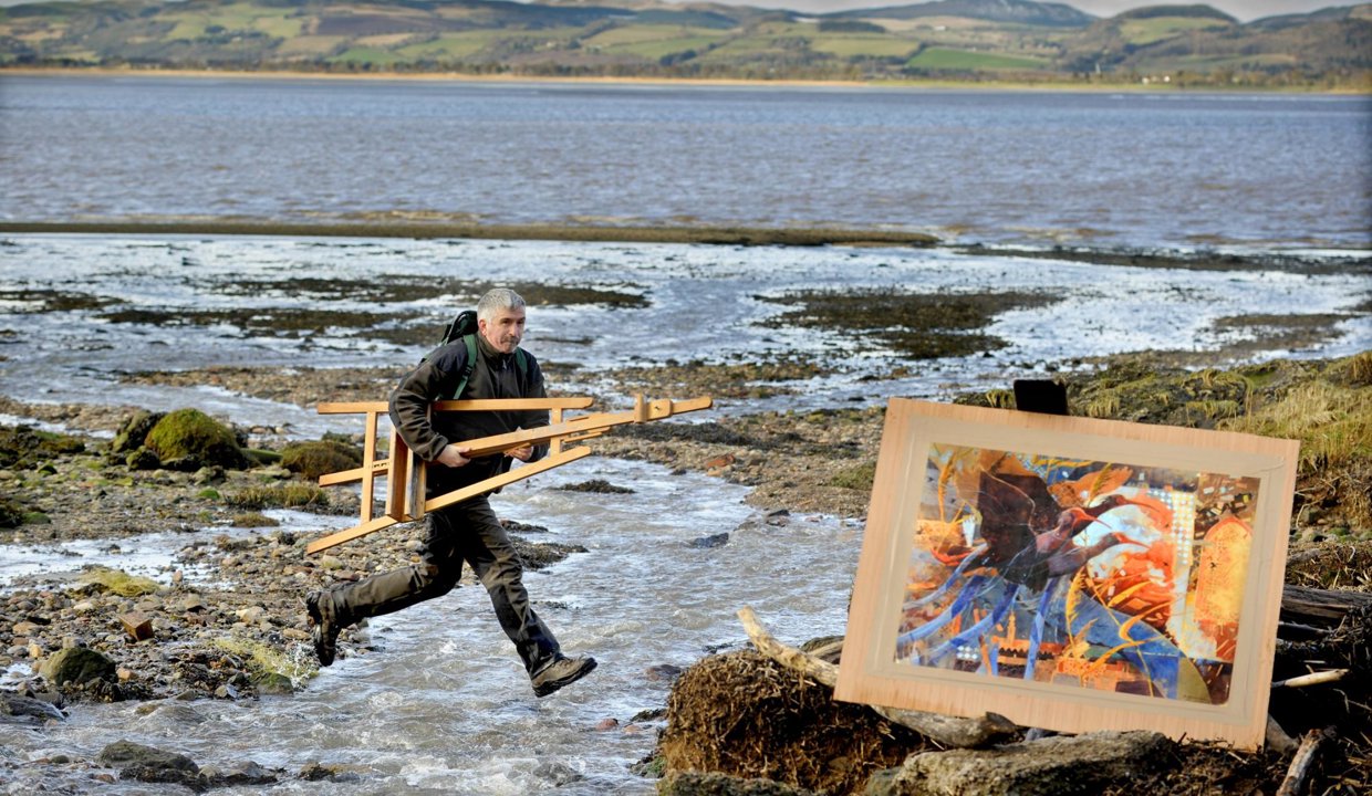 Man at the sea side jumping from rocks holding an easel 