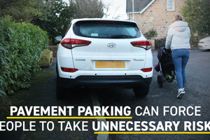 A woman pushing a pram goes onto the road around a car parked on the pavement