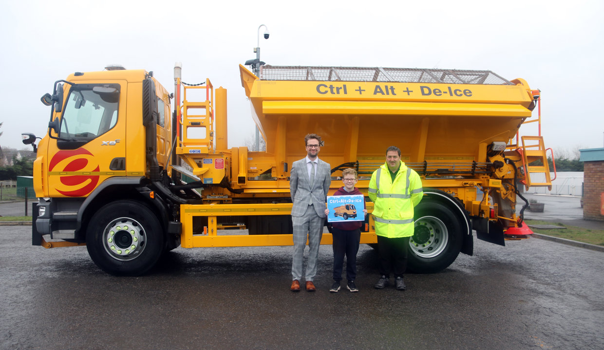 Councillor Paul Ferretti and Fleet manager present winning pupil with a certificate in front of a yellow gritting truck