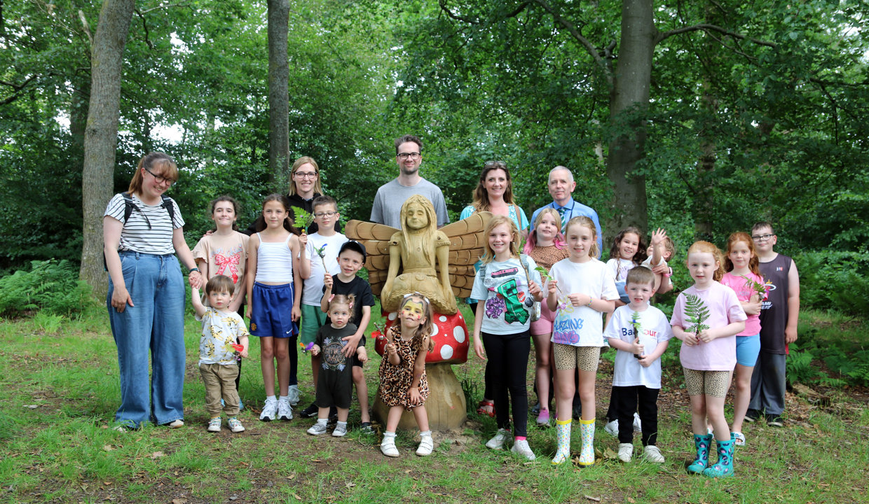 a group of people stand round a wooden statue of a fairy