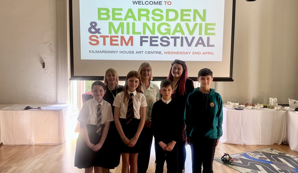 A group of pupils and teachers standing in front of a presentation that says Bearsden and Milngavie stem festival