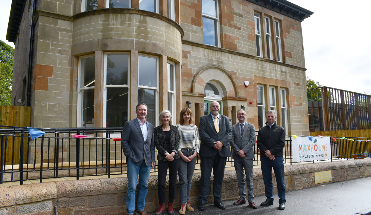 Depute Council Leader Calum Smith standing in the centre of the image outside the front of the newly renovated Brookwood Villa, a two storey blonde sandstone building, flanked by project partners.