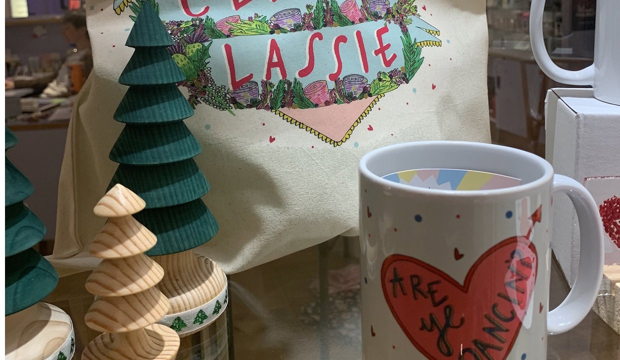 A tote bag with classy lassie and written on it inside a heard with wooden tree ornaments and a mug
