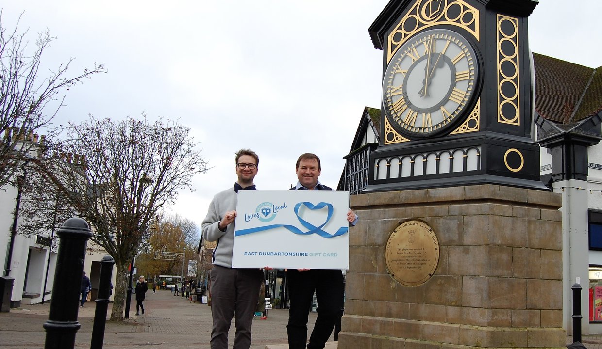 Councillor Paul Ferretti, Convener of East Dunbartonshire Council’s Place, Neighbourhood and Corporate Assets Committee, and Tony IAnson from Milngavie BID standing next to the Milngavie clock while holding a large gift card