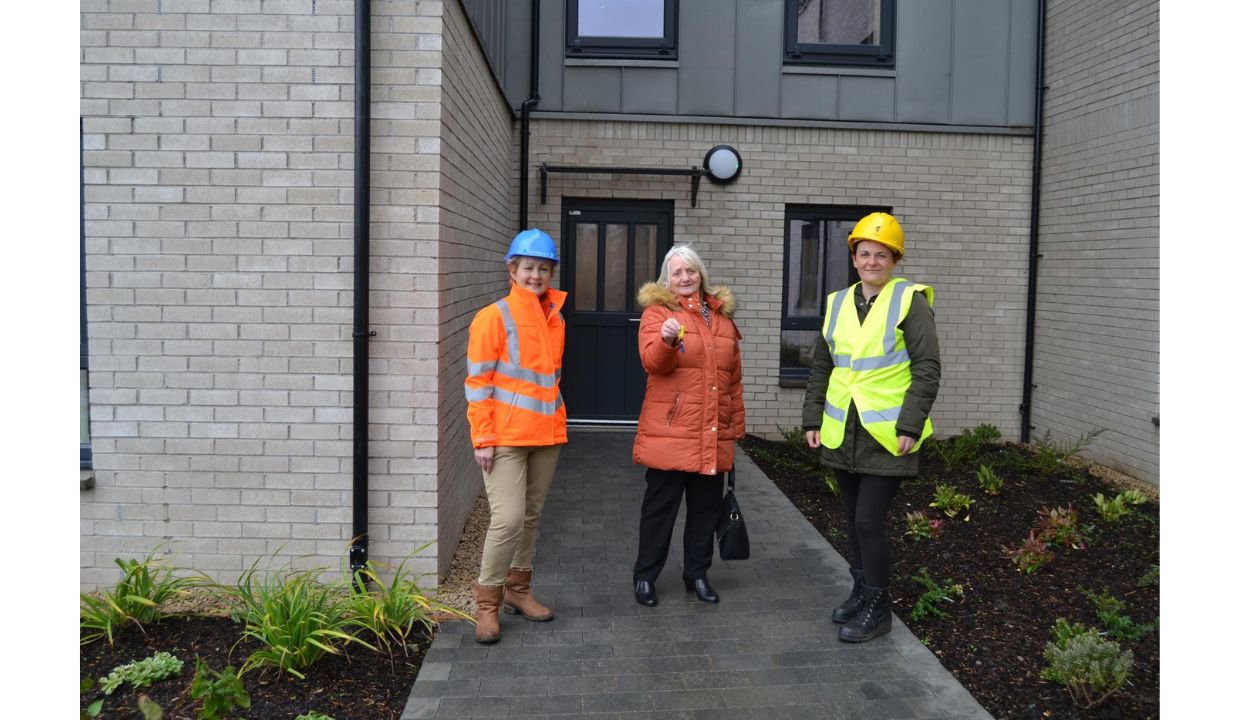 tenant standing outside the new housing with two construction workers in high vis after getting keys to new home