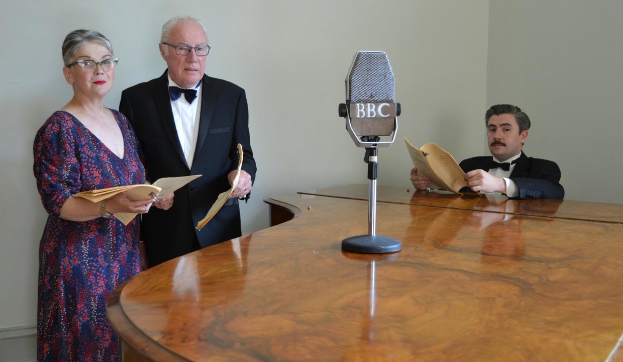 cast of A Christmas Carol; A Radio Play on Stage standing around a microphone holding scripts 