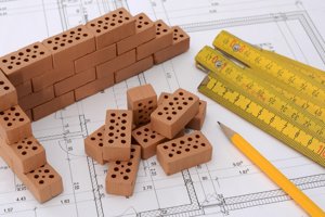 Small bricks, measuring tapes and pencils sitting on top of paper that has illustrations drawn on it