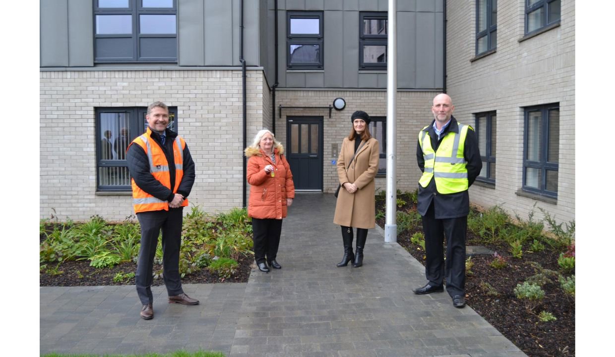 tenant standing outside the new housing with two construction workers in high vis after getting keys to new home