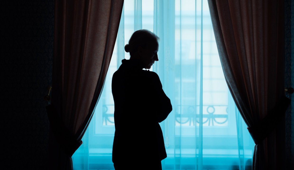 A woman is silhouetted against a window, looking out