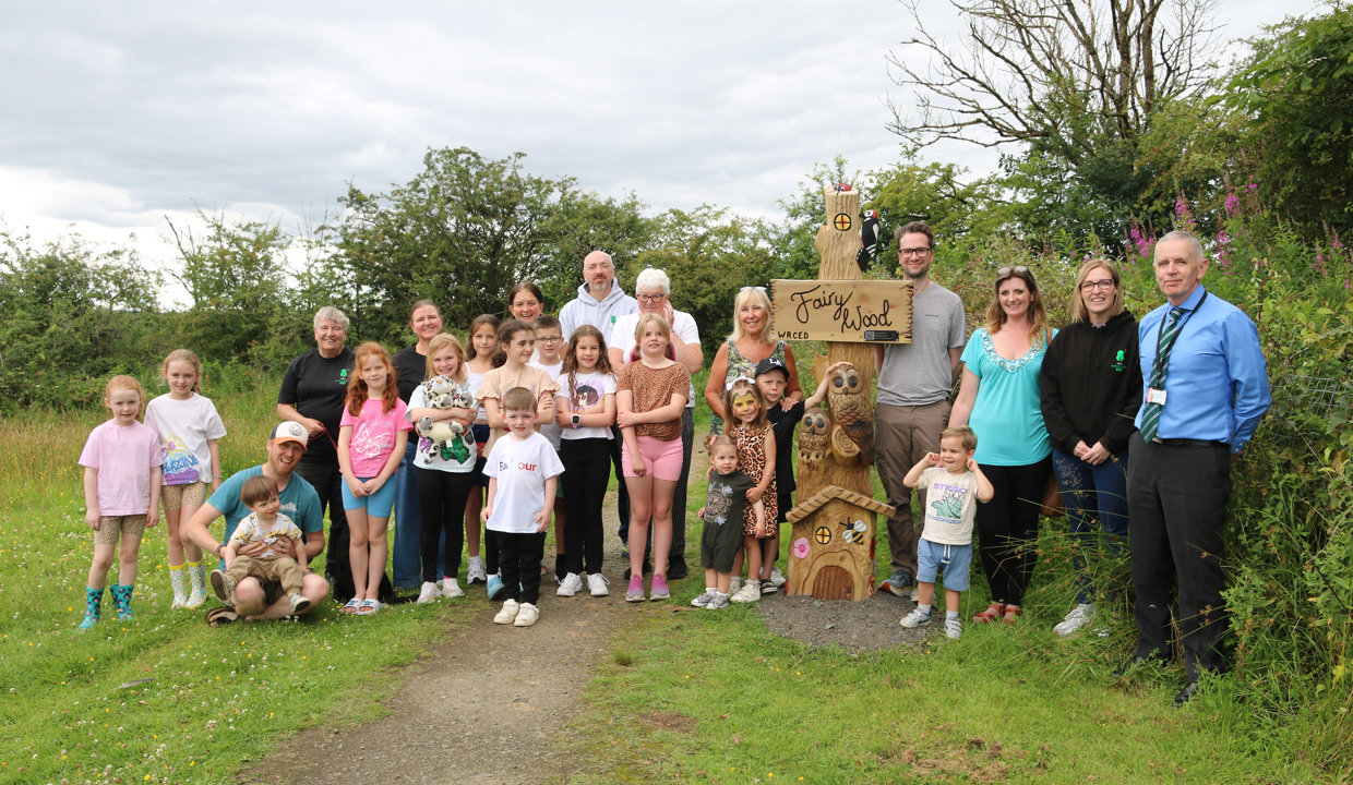 group of people stand round a wooden statue that reads fairy wood