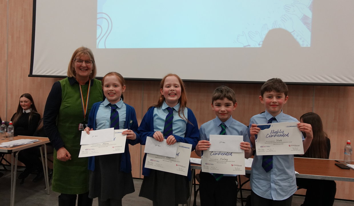 Woman in green dress with four primary school pupils wearing blue school uniforms holding ‘highly commended’ certificates