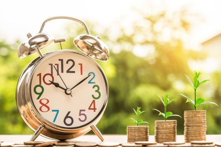 alarm clock with pound coins pilled to the side with plants growing out the top