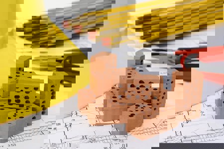 Image of housing bricks, hard hat and pencils on plans