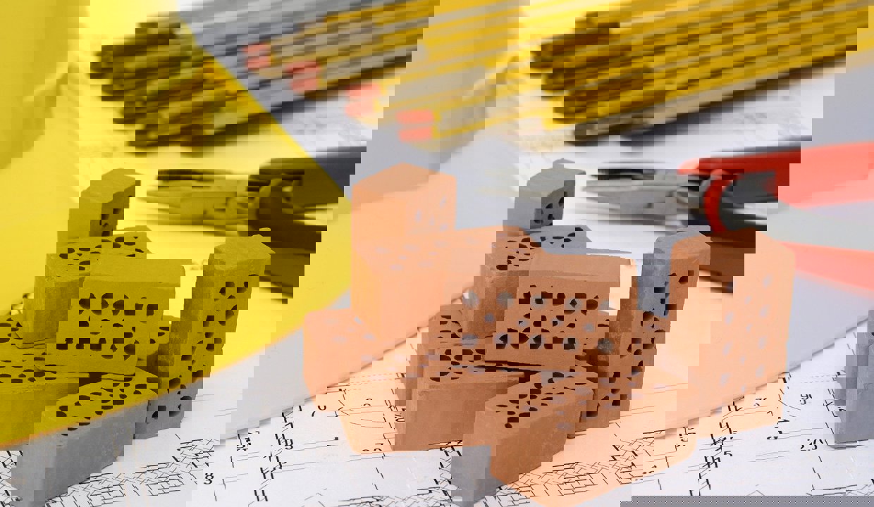 Image of housing bricks, hard hat and pencils on plans