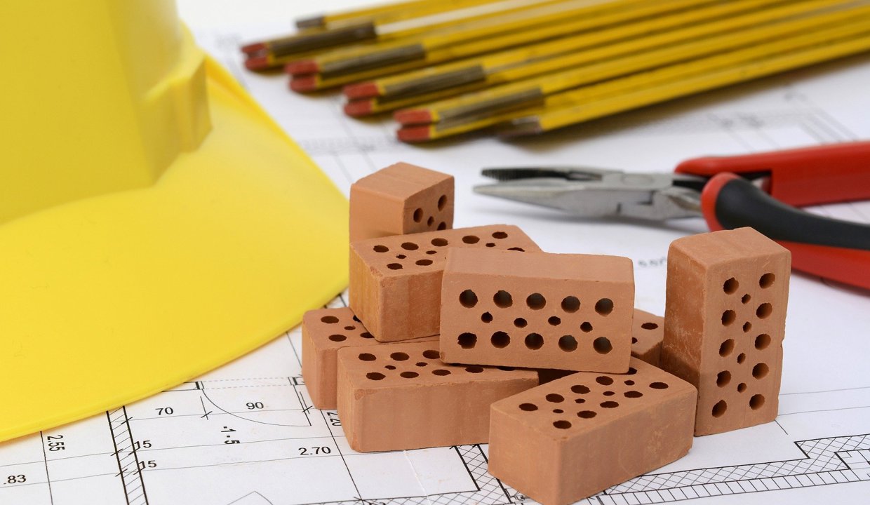 Image of housing bricks, hard hat and pencils on plans