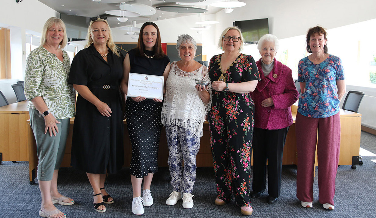 Seven women standing in Council chambers for official photograph.  The woman in the centre is being presented with a framed certificate and a silver quaich. 