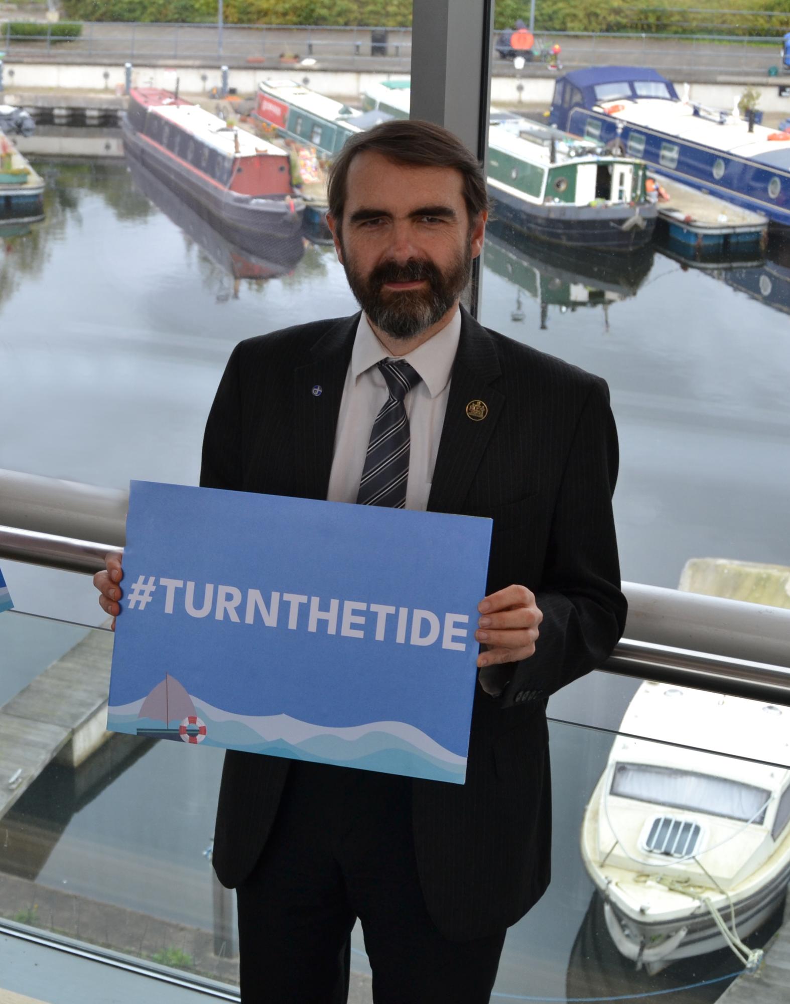 councillor gordan low holding a blue sign that reads #turnthetide
