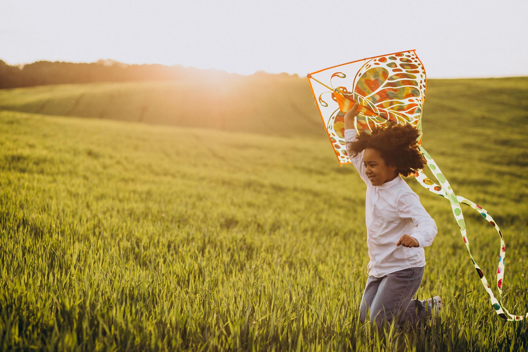 Child flying a kite in a field with the sun setting in the background