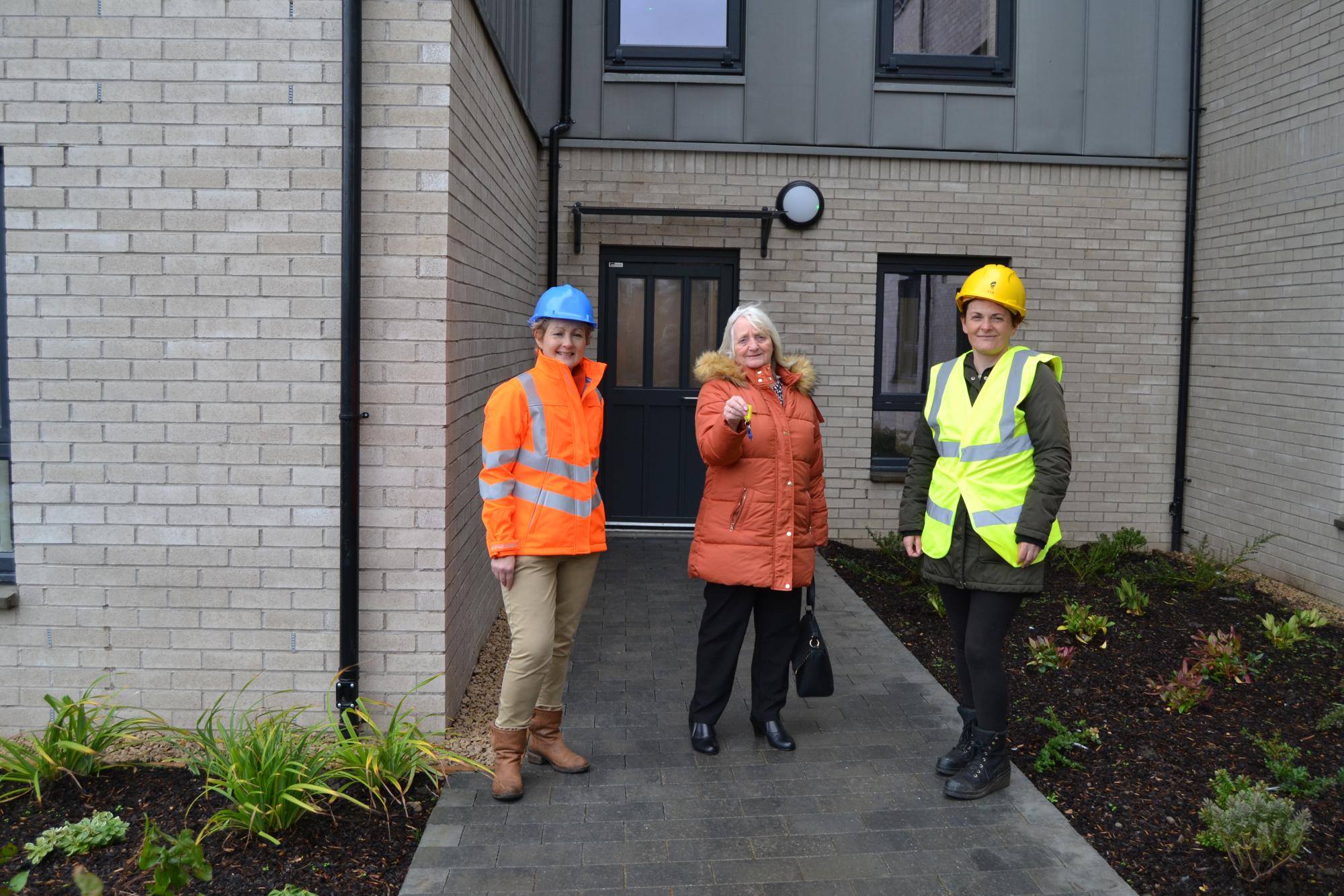 tenant standing outside the new housing with two construction workers in high vis after getting keys to new home