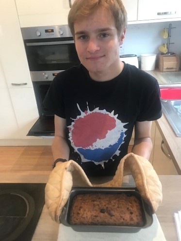 boy in kitchen with oven gloves om holding a baking tray