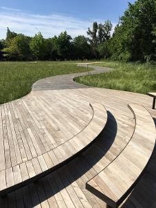 wooden decking with benches next to a grass area with a path that flows through it